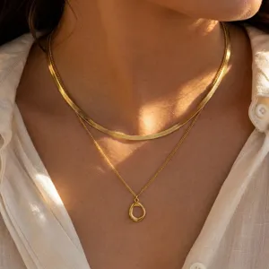 Detailed view of layered minimalist gold herringbone chain and organic oval pendant set