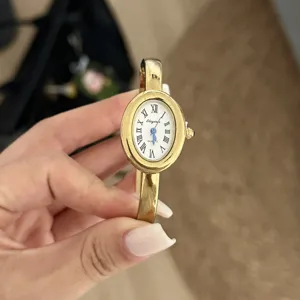Nahaufnahme einer vintage goldenen ovalen Uhr mit römischen Ziffern auf weißem Zifferblatt.