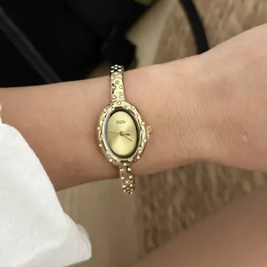 Dettaglio di un orologio da donna dorato con lunetta e cinturino decorati con strass