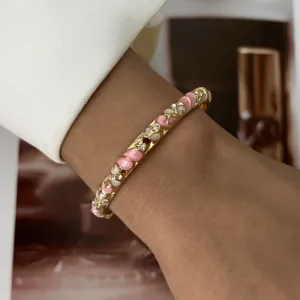 Detail shot of a gold-toned bangle with pink enamel flowers and crystals on a wrist.