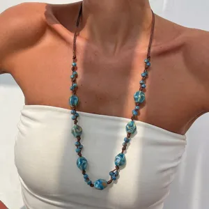Detailed shot of a bohemian blue ceramic bead necklace with brown cord on a white top.