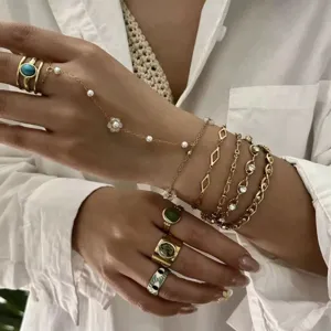 Dettaglio di un set di gioielli dorati con anelli turchesi e catena mano di perle