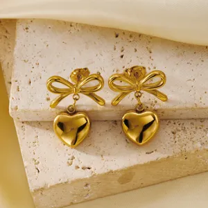 Detailed view of gold bow earrings with heart pendants on a textured stone