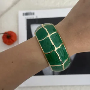Nahaufnahme eines kräftig grünen Emaille-Armreifs mit goldenem Gittermuster am Handgelenk