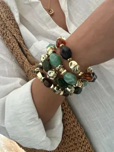 Nahaufnahme von stapelbaren Retro-Armbändern mit unregelmäßigen Acryl- und Goldperlen.