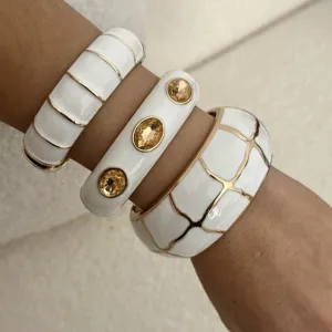 Detailansicht von drei weißen Emaille-Armreifen mit Goldakzenten und Bernsteinsteinen.