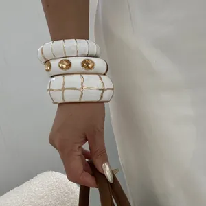 Nahaufnahme von gestapelten weißen Emaille-Armreifen mit goldenen geometrischen Mustern
