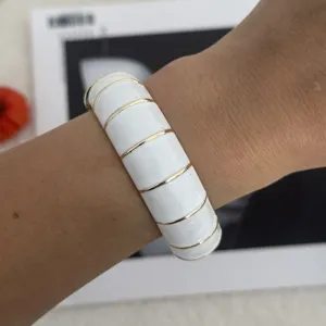 Detailansicht eines Manschettenarmbands mit weißer Emaille und goldfarbenen Streifen am Handgelenk.
