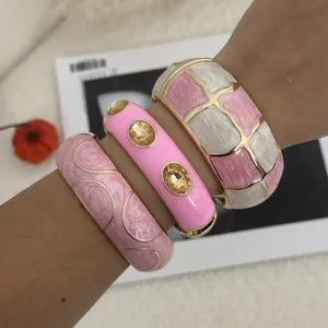 Nahaufnahme von klobigen rosa-weißen Emaille-Armreifen mit bernsteinfarbenen Kristallen