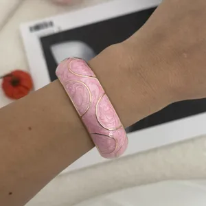 Detailaufnahme eines pinkfarbenen Emaille-Armreifs mit goldenen geometrischen Wellenmustern