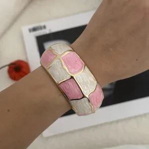 Detailansicht eines rosa-weißen Emaille-Armreifs mit Schachbrettmuster am Handgelenk