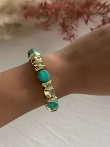 Detailansicht eines Armbands mit klobigen goldenen und türkisen Acrylperlen am Handgelenk.