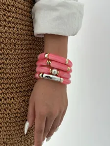 Dettaglio di eleganti bracciali a tubo in acrilico rosa con accenti dorati e perla