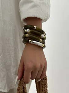 Dettaglio di bracciali impilati in acrilico verde oliva con perle e oro