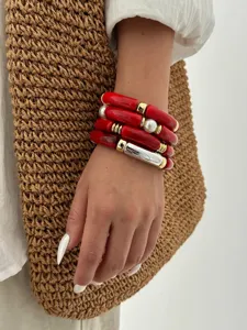 Primo piano di bracciali a tubo in acrilico rosso con perle e dettagli dorati