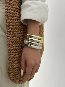 Dettaglio di bracciali a tubo in acrilico a strati con finiture oro, argento e perle.