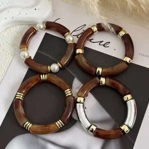 Dettaglio dei braccialetti in acrilico ambrato stile Maillard con accenti dorati
