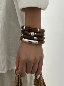Dettaglio di bracciali in tubo di acrilico marrone stile Maillard con accenti oro e perle.