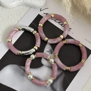 Primo piano di braccialetti a tubo in acrilico rosa marmo con accenti dorati e perle