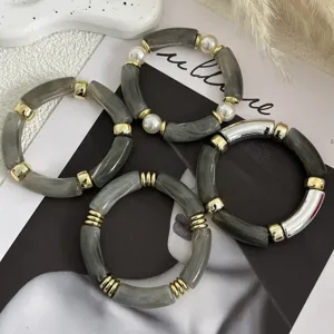 Dettaglio di braccialetti in acrilico grigio marmorizzato con finiture in oro.