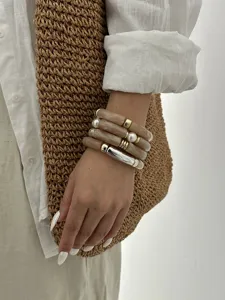 Dettaglio di bracciali a tubo in acrilico con perle e accenti metallici sul polso