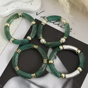 Dettaglio dei braccialetti in acrilico verde marmorizzato con finiture oro e perle