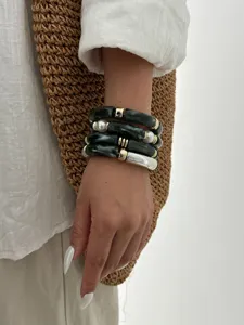 Dettaglio di bracciali sovrapposti in acrilico con trama marmorizzata e perle bianche
