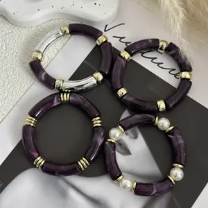 Dettaglio di bracciali in acrilico viola con accenti dorati e perle eleganti