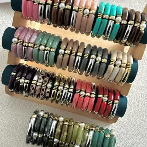 Bracciali a tubo di bambù in acrilico colorato con perle e accenti dorati su supporto in legno