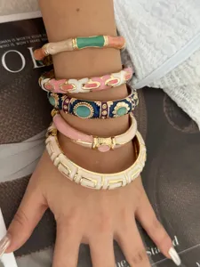 Close-up of layered colorful enamel bamboo-joint and geometric bangles on a female wrist.