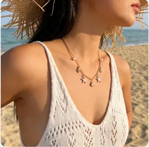 Detail view of gold vacation necklace with starfish and shell charms on model at beach