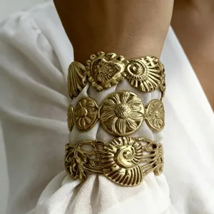 Dettaglio di tre bracciali rigidi in acciaio inossidabile dorato con motivi floreali