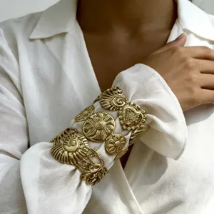 Primo piano di un bracciale rigido dorato inciso indossato sopra una camicia bianca