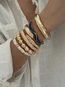 Detailaufnahme gestapelter Vintage-Armreifen mit buntem Emaille und Goldtexturen.