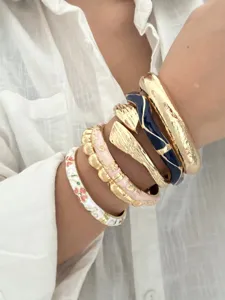 Detailansicht von gestapelten Retro-Armbändern mit Gold- und Emaille-Texturen am Handgelenk