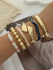 Nahaufnahme von stapelbaren Vintage-Emaille-Blumen- und Gold-Strukturarmreifen am Handgelenk