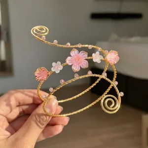 Dettaglio macro di un bracciale da braccio in filo dorato con fiori rosa e conchiglie.
