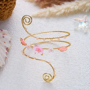 Dettaglio del bracciale da braccio a spirale dorata con fiori rosa su sfondo di sabbia.