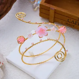 Dettaglio macro di un bracciale da braccio dorato regolabile con fiori rosa e conchiglie.