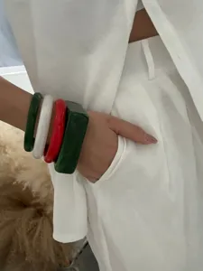 Detailansicht bunter geometrischer Harzarmbänder in Grün, Weiß und Rot auf weißem Outfit