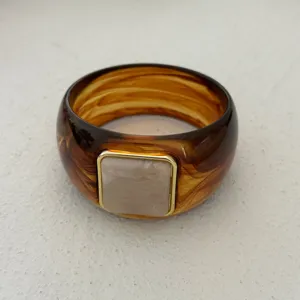 Nahaufnahme eines bernsteinfarbenen Harzarmreifs mit quadratischem rosa Inlay und Goldrand