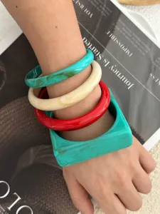 Nahaufnahme eines Sets aus vier Acrylarmreifen in Blaugrün, Creme und Rot am Handgelenk