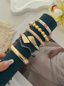 Nahaufnahme von Vintage-Gold- und Emaille-Armreifen auf einem grünen Samtständer