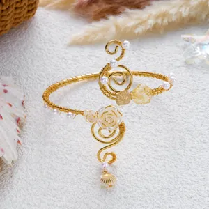Vista dettagliata di un bracciale da braccio dorato con conchiglia, rosa e perle sulla sabbia.