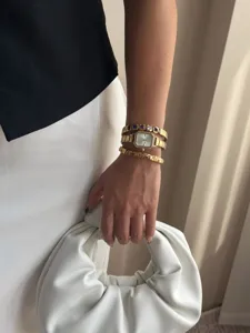 Nahaufnahme einer eleganten goldenen quadratischen Uhr und Edelsteinarmbänder