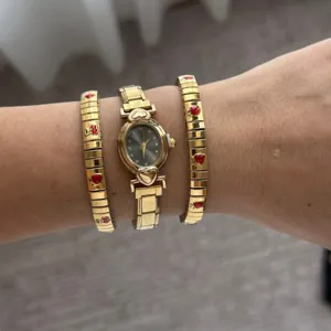 Elegant oval watch with matching golden bracelets featuring red heart charms on wrist