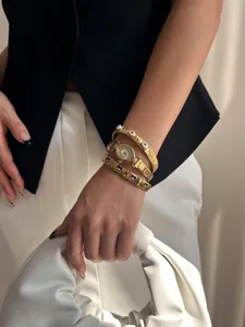 Close-up view of gold evil eye watch and elastic link bracelets set worn on female wrist