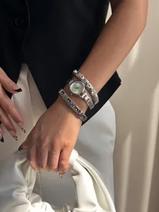 Detail view of silver evil eye watch styled with matching heart charm bracelets.