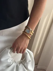 Nahaufnahme einer eleganten goldenen Quarzuhr und bunter Edelsteinarmbänder am Handgelenk