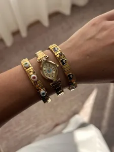 Close-up of gold evil eye marquise watch stacked with link charm bracelets on wrist